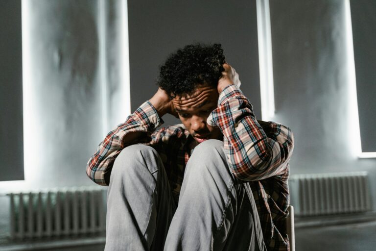 A man sitting with his hands on his head, appearing anxious and distressed.